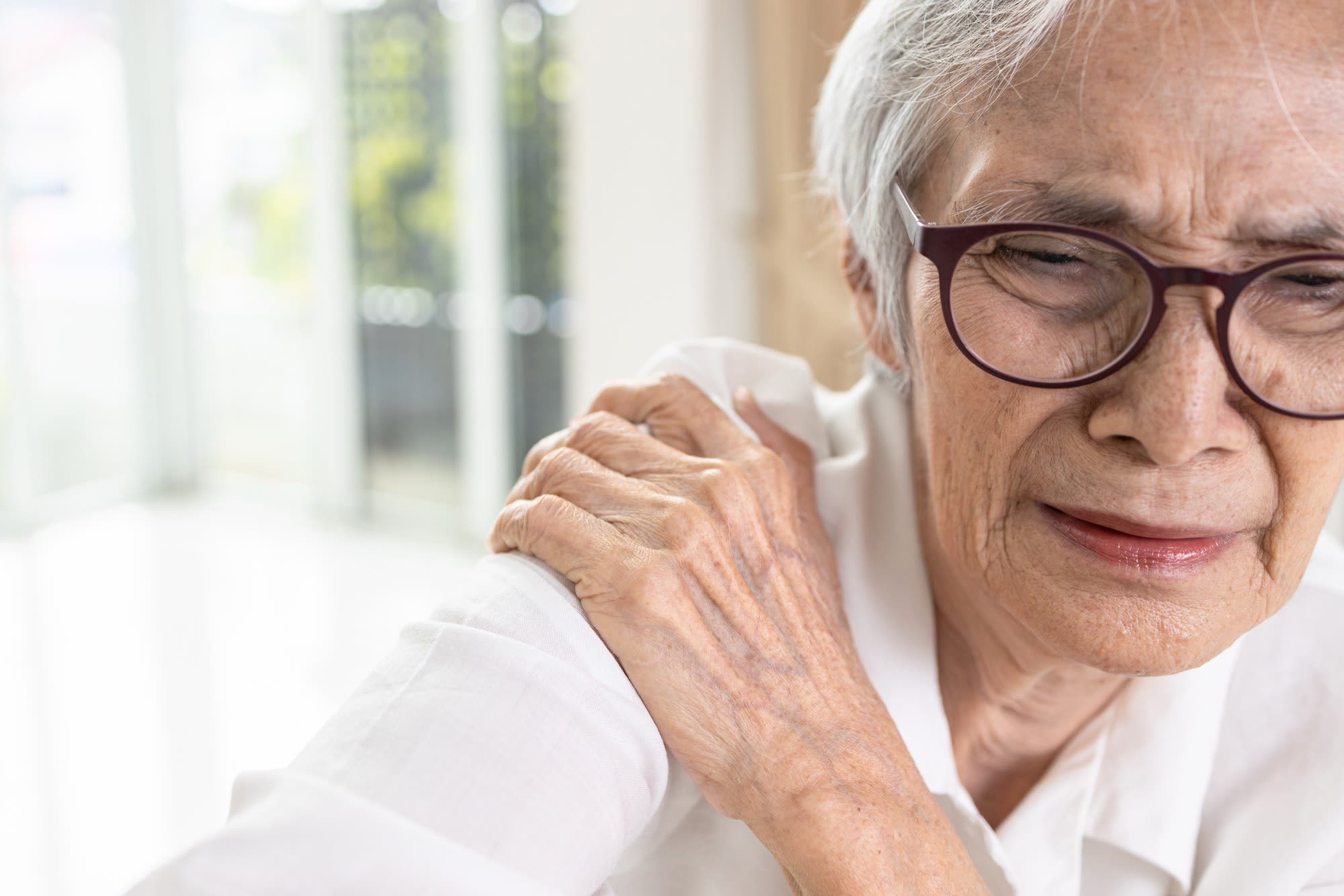 An older woman grips her painful shoulder