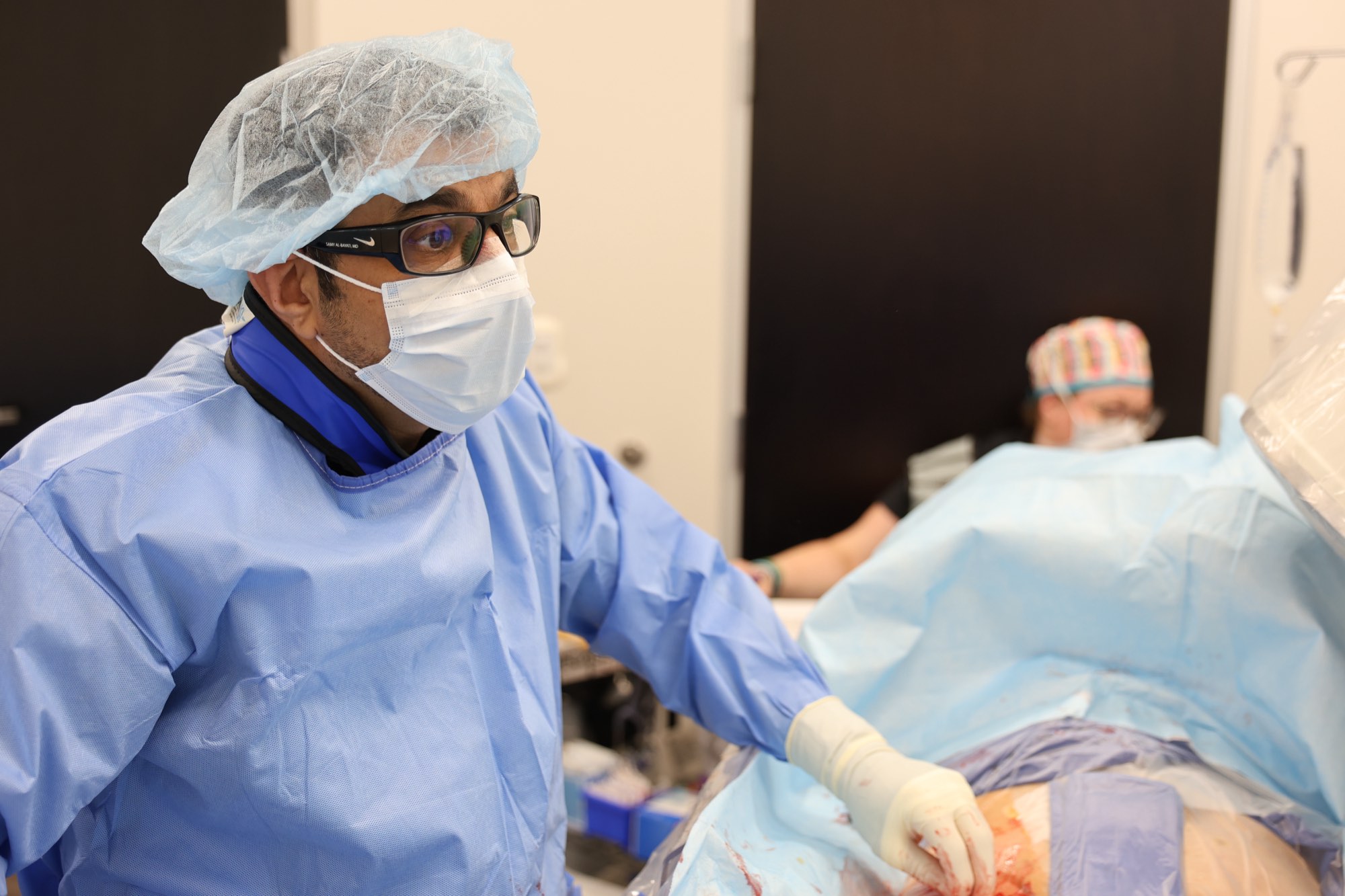 Dr. Samy Al-Bayati, in surgical cap and mask, performs an image-guided procedure in the ARVC interventional radiology suite