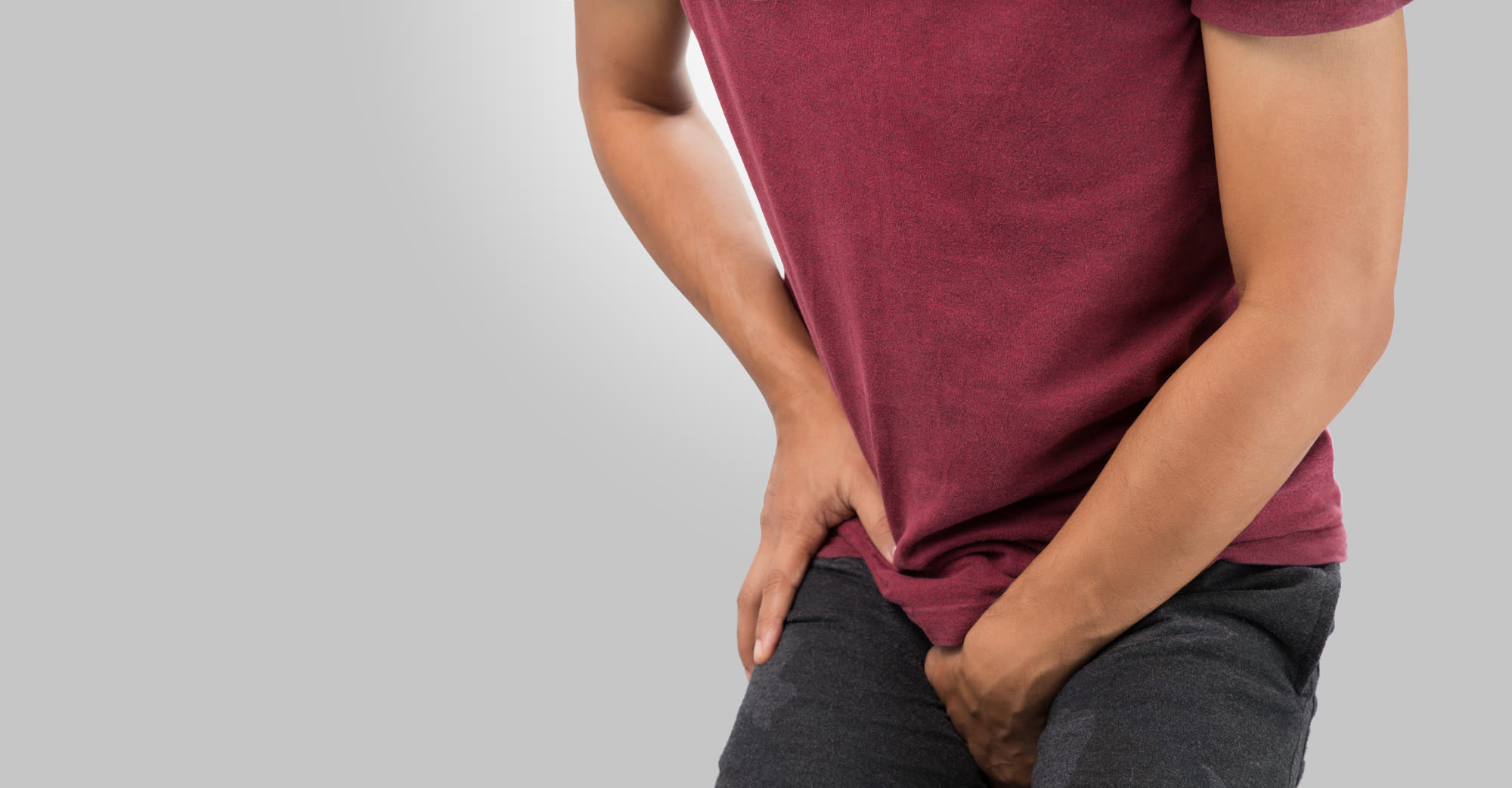 A man in a red T-shirt holding his groin in discomfort