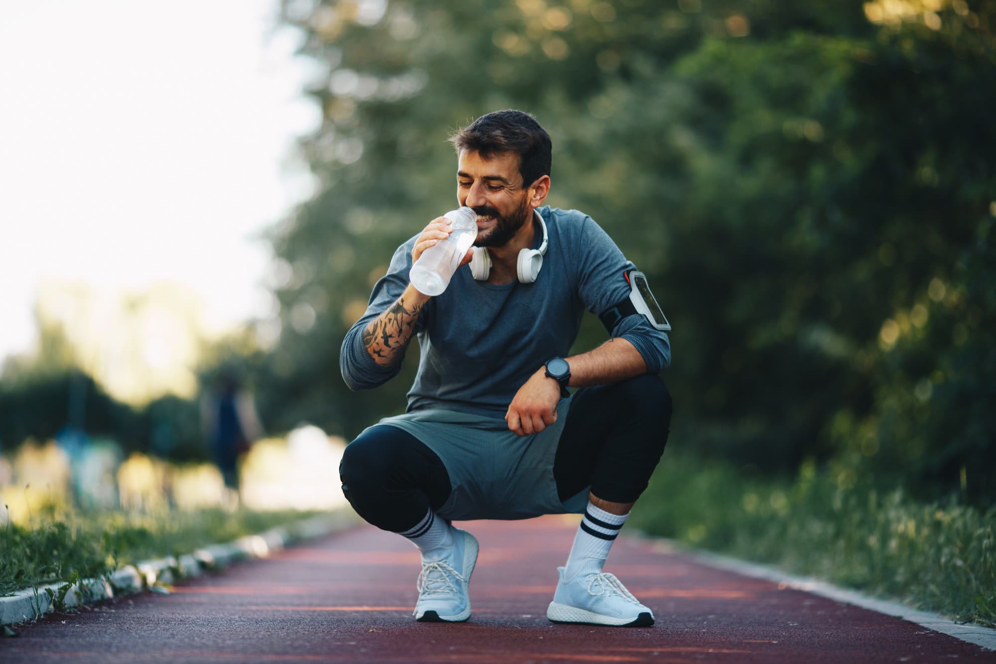 A man in his thirties pausing for water on a running track after exercise