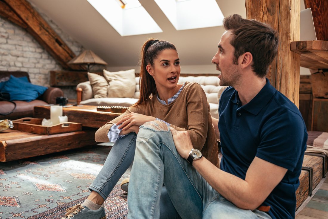 A couple sitting on the floor of their living room, talking seriously