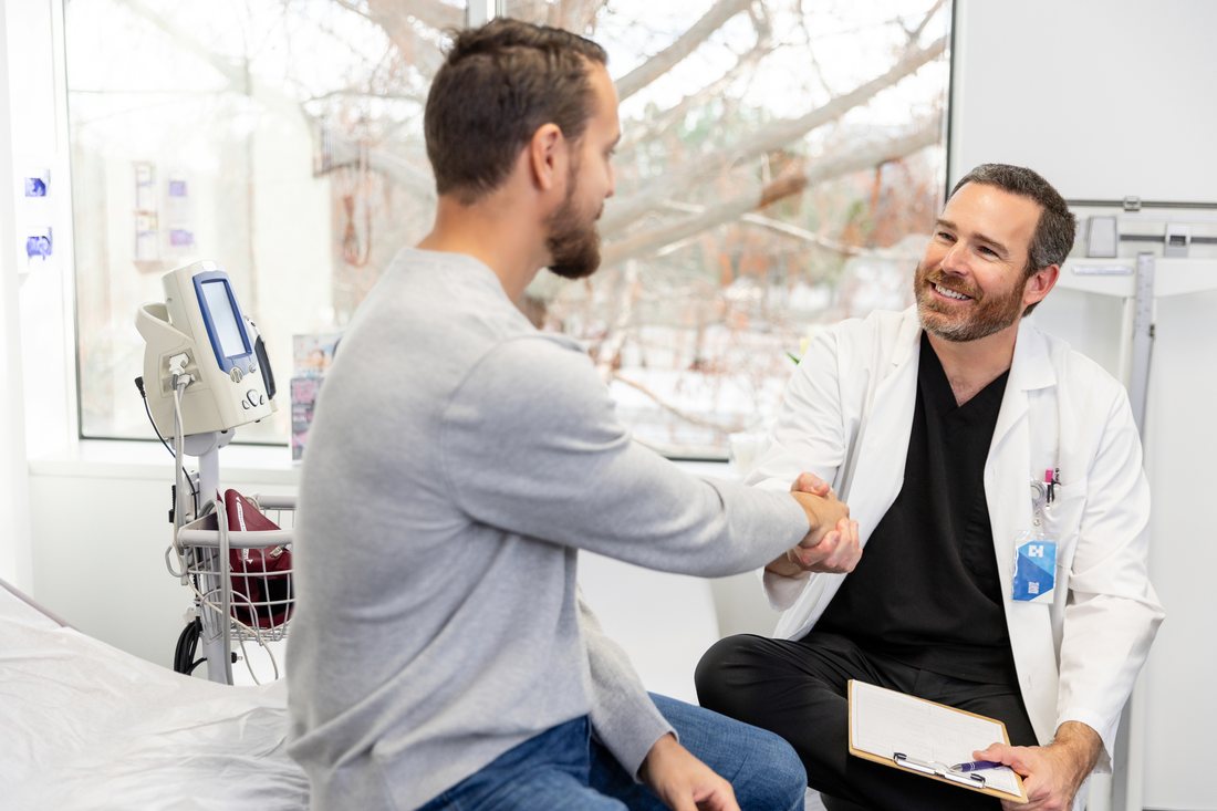 A doctor in a white coat shaking hands with a patient in an exam room