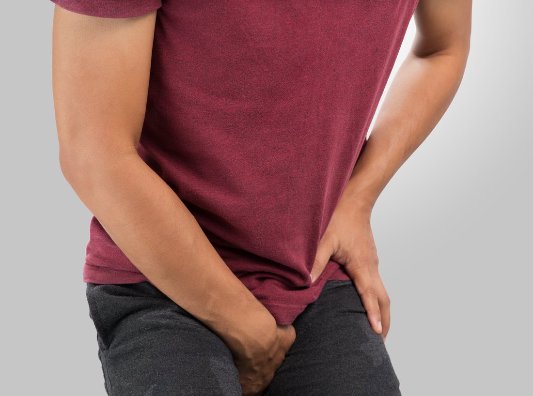 A man in a t-shirt standing with one hand pressed low against his groin