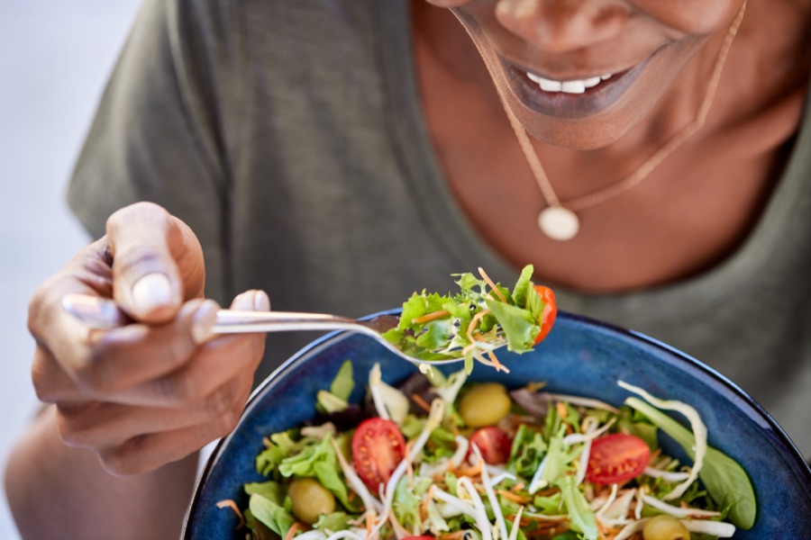 A woman eating a fresh salad of leafy greens, tomatoes and sprouts from a bowl