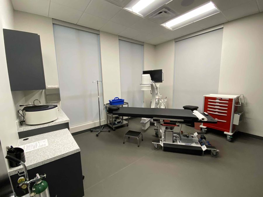 The procedure room at ARV Centers: a procedure table with a C-arm X-ray unit and monitor beside it, under natural light