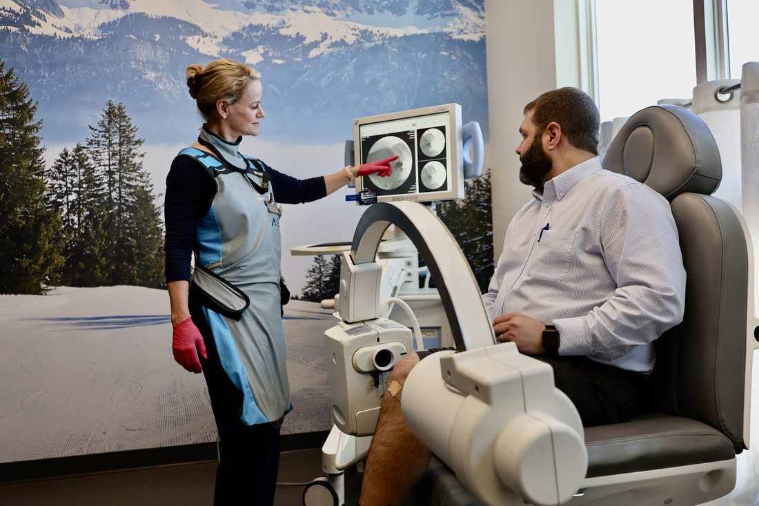 Dr. Lisa Persyn, in a lead apron, pointing to live fluoroscopic images of a knee on the C-arm monitor in the ARV Centers procedure suite