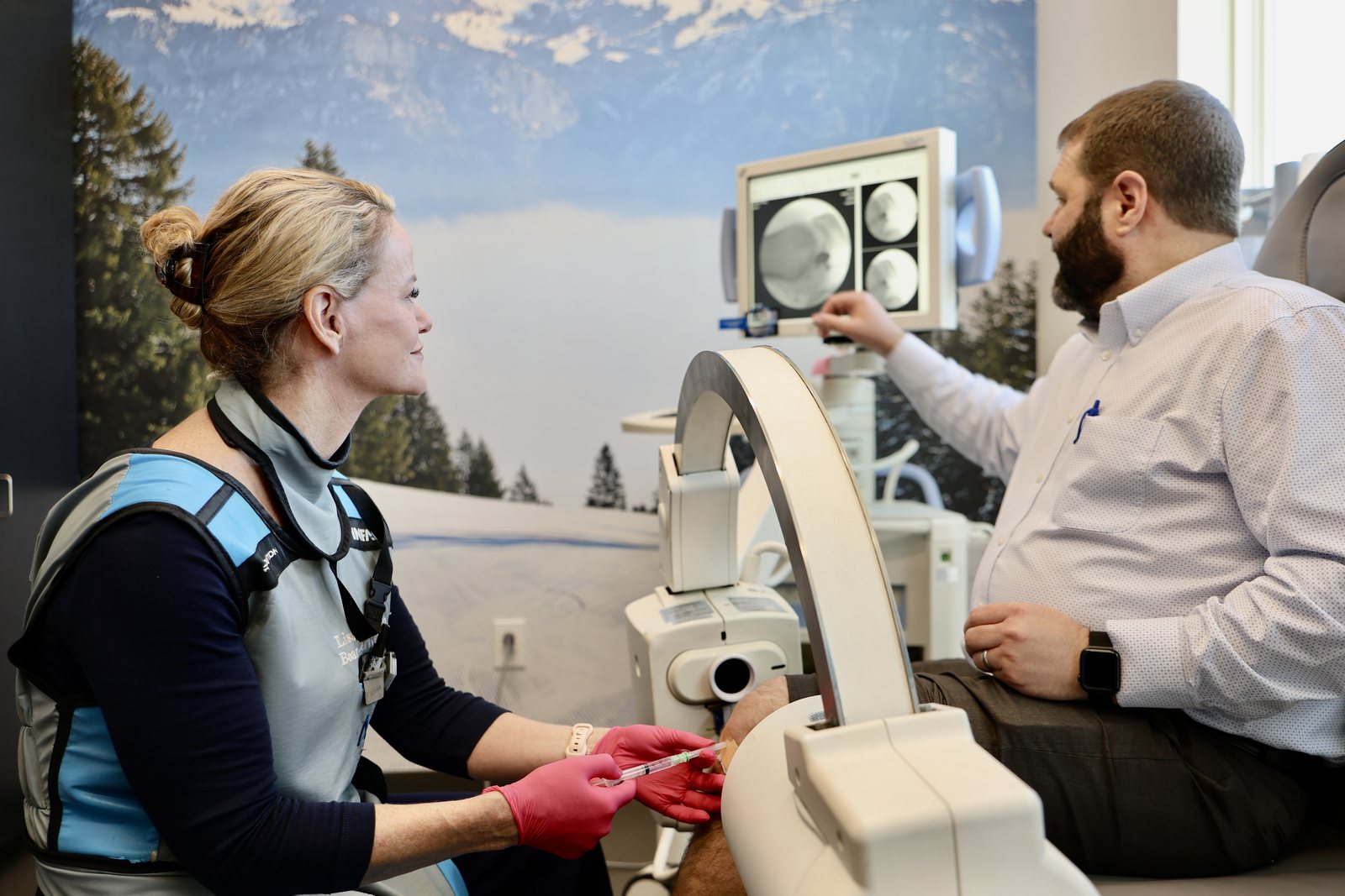Lisa D. Persyn, M.D. performing an image-guided knee injection at ARV Centers in San Antonio while the patient points to his own knee on the live fluoroscopy screen