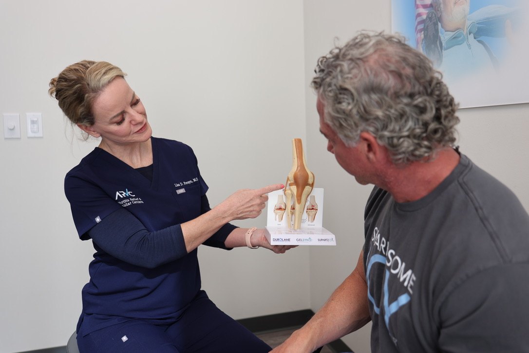 Dr. Lisa Persyn in ARV Centers scrubs, pointing to a knee model as she talks a patient through the gel injection options