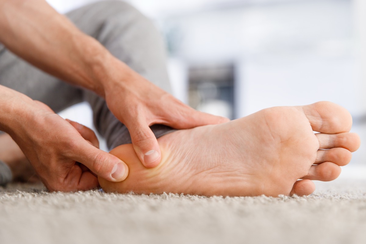 A person sitting on the floor pressing both thumbs into the arch and heel of their bare foot
