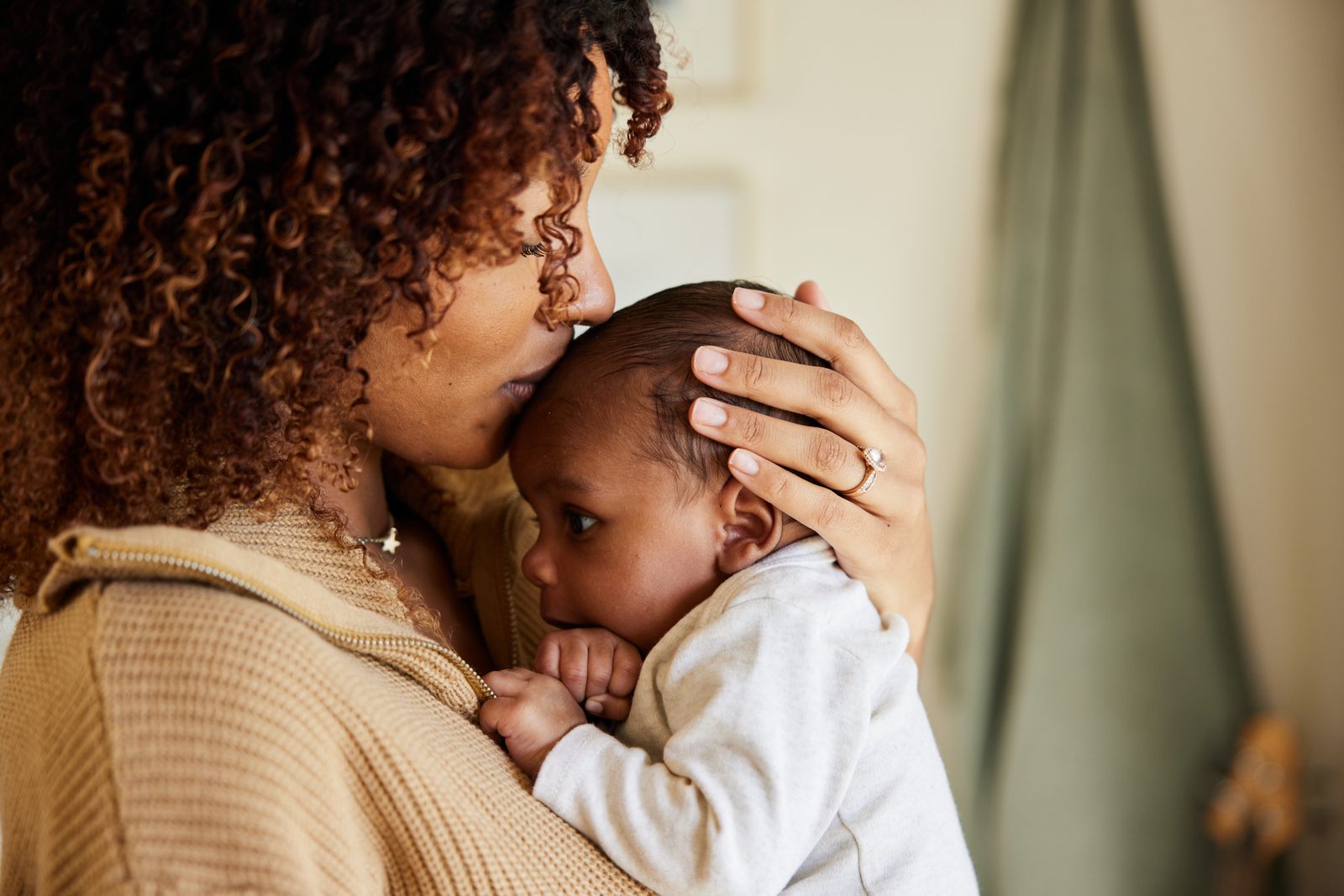 A mother holding her baby close, kissing the top of the baby&rsquo;s head